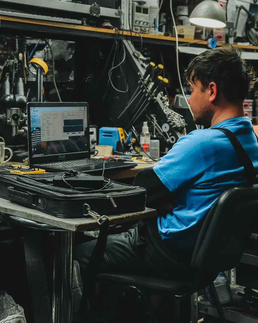 Technician working at a laptop on a workshop bench surrounded by tools and equipment